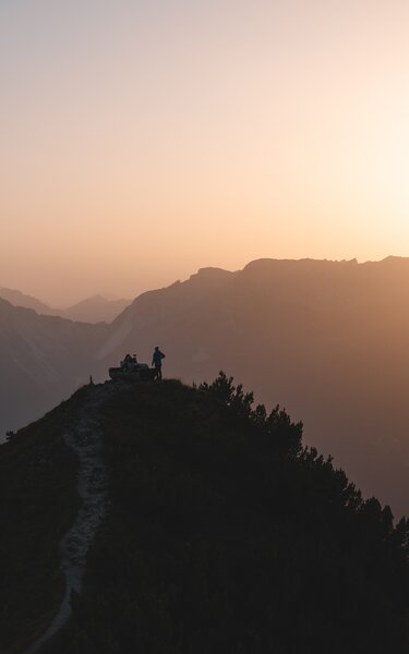 Sonnenuntergang Gratlspitze | © Alpbachtal Tourismus | Mathäus Gartner Zwei Menschen sitzen auf der Rastbank Gratlspitze und genießen den Sonnenuntergang, welcher in schönen Farben zu sehen ist | © Alpbachtal Tourismus | Mathäus Gartner