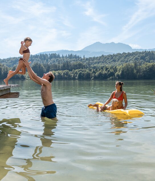 Vater hebt seinen Sohn vom Steg in den Reintalersee, die Mutter wartet bereits im Wasser mit dem Sohn auf einer Luftmatratze  | © Alpbachtal Tourismus 