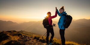 Zwei Frauen geben sich ein High 5 auf dem Wiedersberger Horn, währenddessen im Hintergrund der schöne Sonnenaufgang  | © Alpbachtal Tourismus | shootandstyle