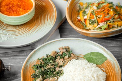 Ein Teller mit Reis und hellem Curry steht auf einem Tisch mit einem Salatteller und einem Saftglas. | © freepik