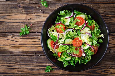 Eine Schüssel mit Blattsalat, Tomaten und Gurken mariniert steht auf einem Holztisch. | © freepik