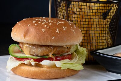 Ein Burger gefüllt mit Fleisch, Käse, Tomaten und Gurken auf einem Teller garniert mit Pommes frites. | © David Foodphototasty | Unsplash