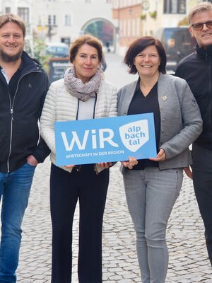 Der operative Vorstand der WiR Alpbachtal, zwei Männer und zwei Frauen, stehen gemeinsam im Stadtzentrum von Rattenberg und halten ein blaues Schild mit der Aufschrift "WiR Alpbachtal" in den Händen. | © WiR Alpbachtal