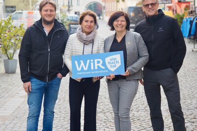 Der operative Vorstand der WiR Alpbachtal, zwei Männer und zwei Frauen, stehen gemeinsam im Stadtzentrum von Rattenberg und halten ein blaues Schild mit der Aufschrift "WiR Alpbachtal" in den Händen. | © WiR Alpbachtal
