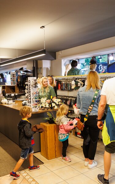 Personen, Männer, Frauen und Kinder, gehen durch das Geschäft von Connys Sport und Mode Brixlegg, zwei Verkäuferinnen stehen bei der Kassa. | © WiR Alpbachtal | Maximalgrafik