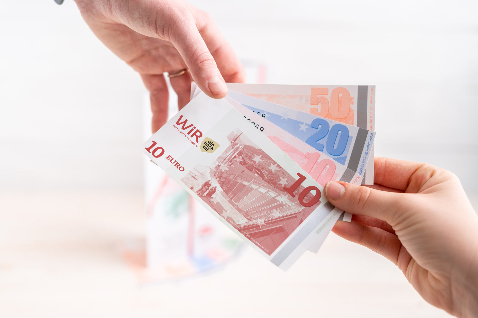 Nahaufnahme von zwei Händen, die gemeinsam WiR-Gutscheine halten. | © WiR Alpbachtal | Genusskind