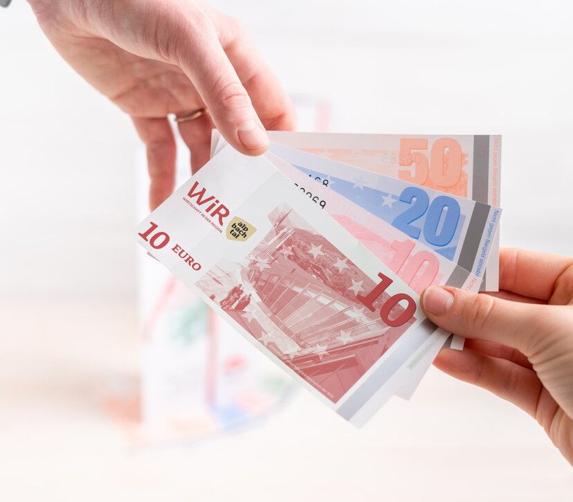 Nahaufnahme von zwei Händen, die gemeinsam WiR-Gutscheine halten. | © WiR Alpbachtal | Genusskind