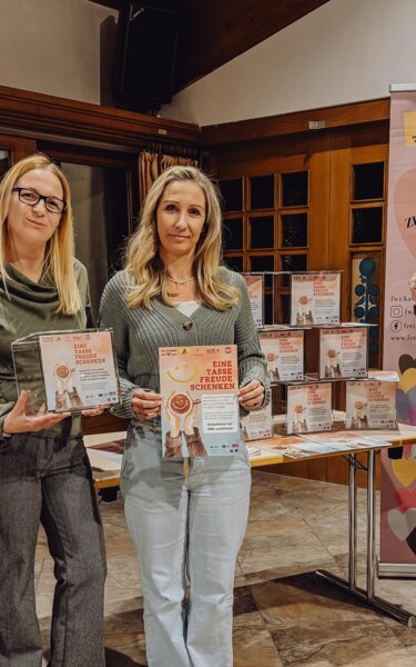Pressefoto Eine Tasse Freude schenken | © WiR Alpbachtal 5 Frauen stehen vor einem Tisch mit Plexiglasboxen und einem Roll-up des Freiwilligen Zentrum Kitzbüheler Alpen, zwei Frauen halten ein Plakat des Projekts "Eine Tasse Freude schenken" in der Hand, eine Frau eine Plexiglasbox für die Gutscheinsammlung. | © WiR Alpbachtal