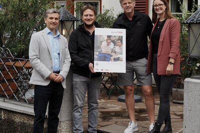 Drei Männer und eine Frau stehen vor dem Gasthof Herrnhaus in Brixlegg und halten gemeinsam eine Tafel mit der Aufschrift "Digital-Lotsen-Programm Tirol". | © WiR Alpbachtal
